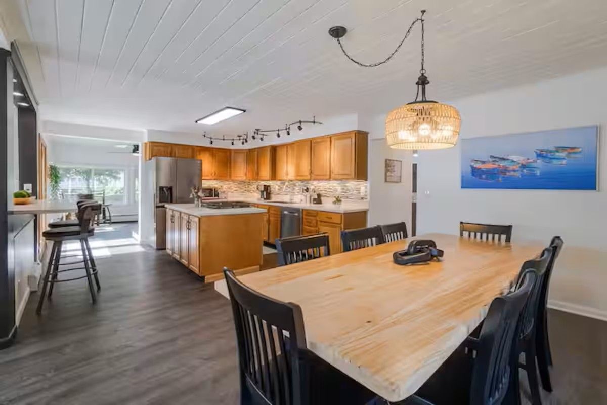Una cocina moderna con armarios de madera, una isla central y un comedor con mesa y sillas de madera.