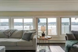 A room with a sofa and a lamp, large windows with a view of a body of water and hills.