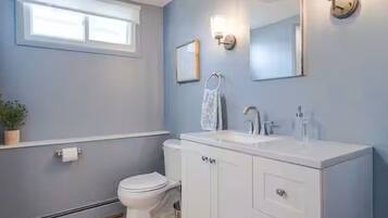 Un baño con inodoro, lavamanos blanco y espejo.