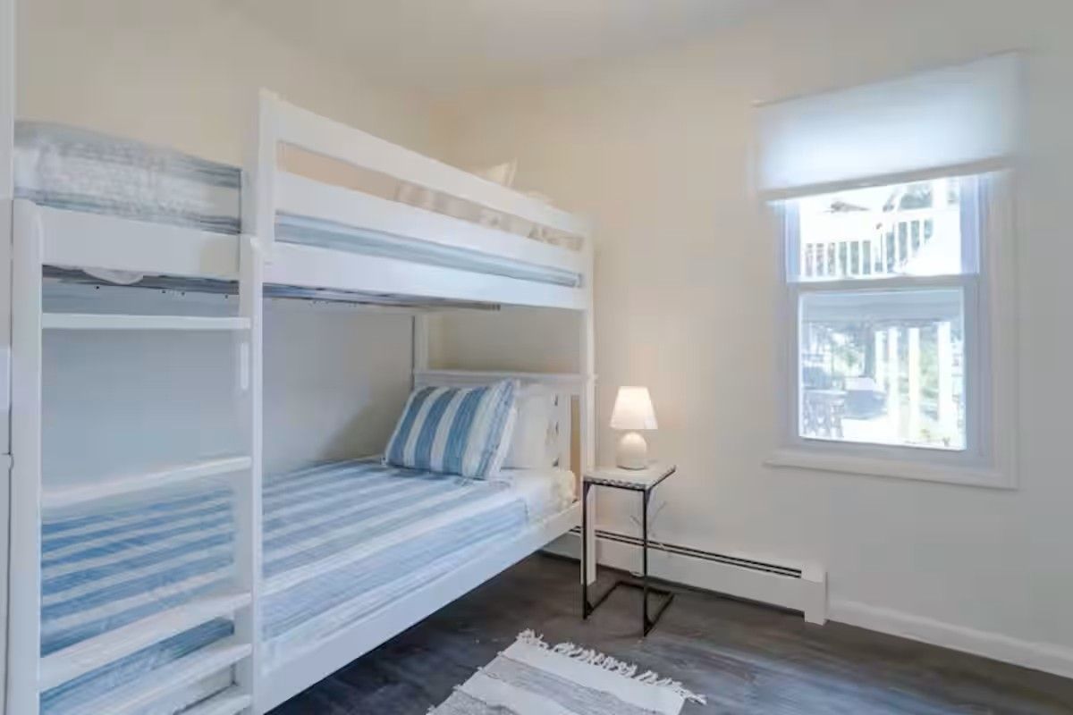Ein Zimmer mit Etagenbetten, einem kleinen Tisch mit Lampe und einem Fenster mit Blick.