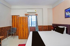 Hotellihuone, jossa on sänky, tuoli, vaatekaappi ja ikkuna, jossa on verhot.