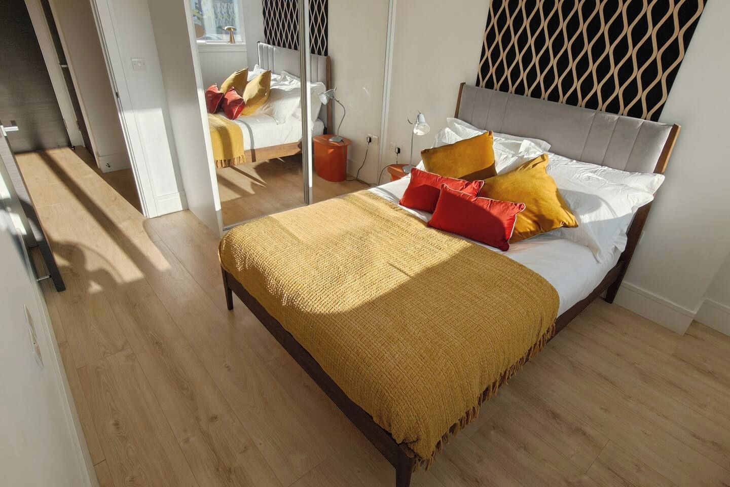 A bedroom with a bed, a mirror, and a wooden floor.