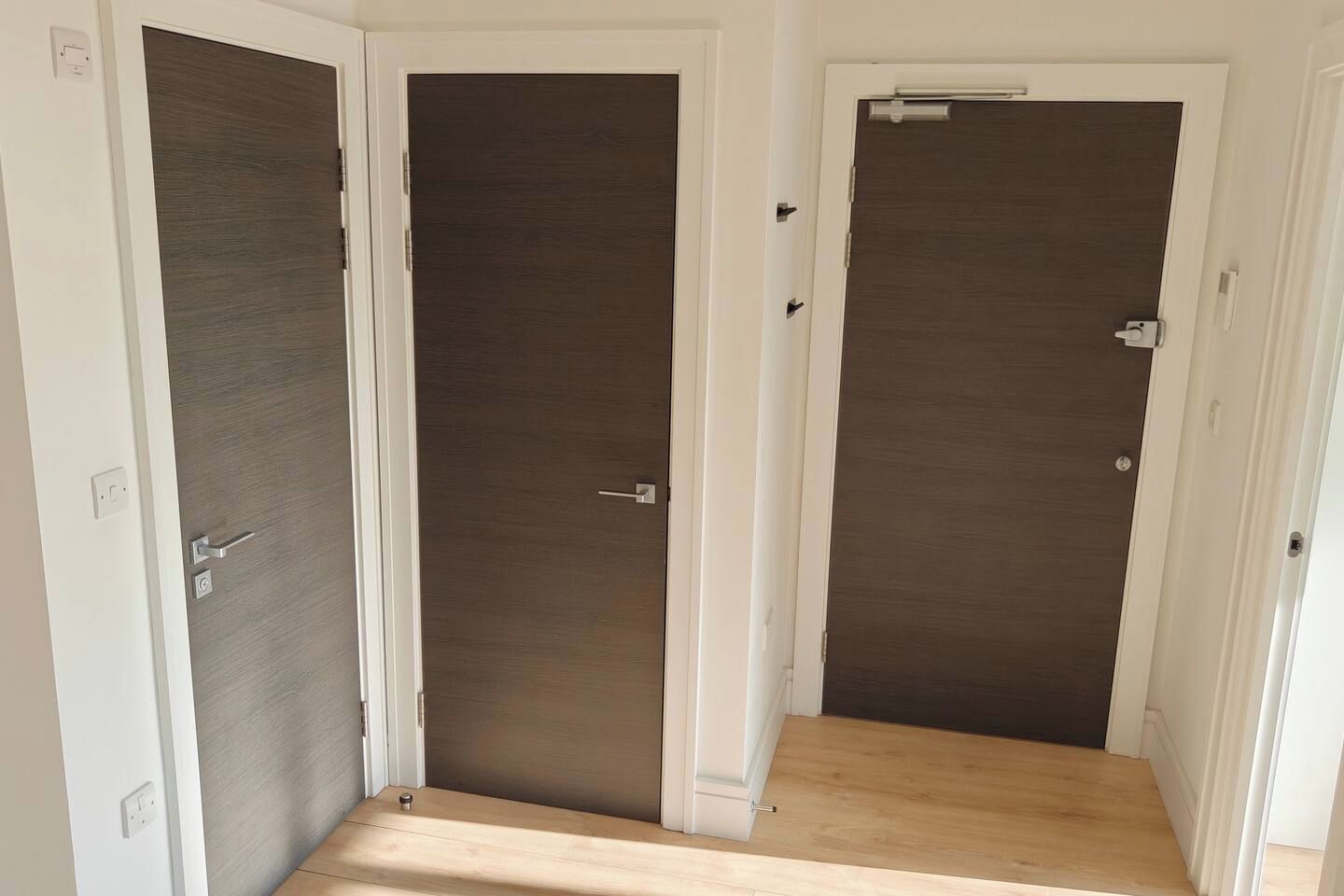 A hallway with three closed doors, a light switch, and a power outlet on the wall.