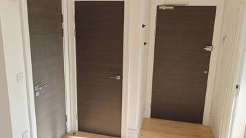 A hallway with three closed doors, a light switch, and a power outlet on the wall.