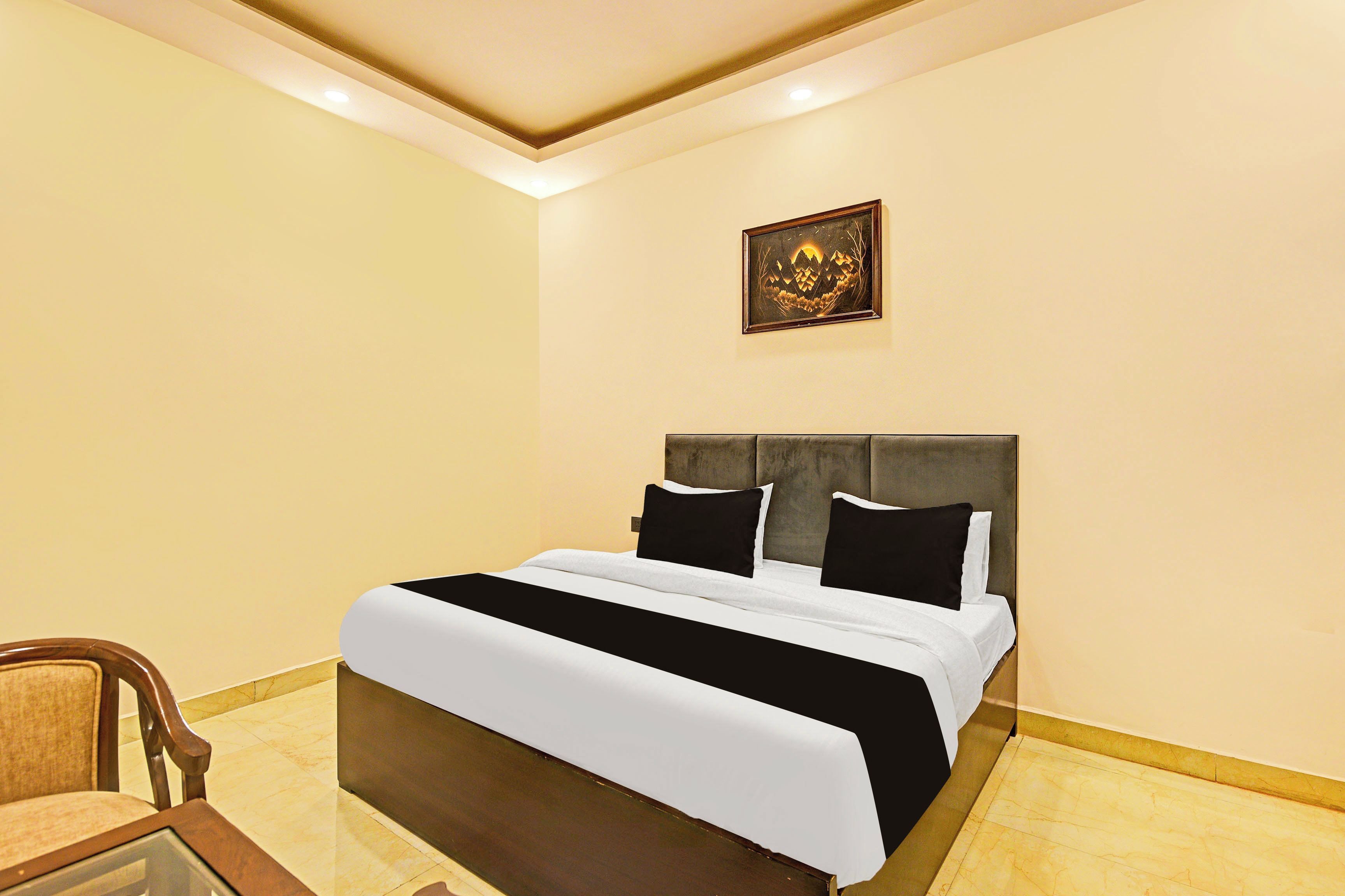 A hotel room with a bed, a chair, and a framed picture on the wall.