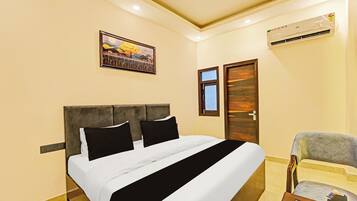 Habitación de hotel con una cama, una silla, un equipo de aire acondicionado, una puerta y un cuadro en la pared.
