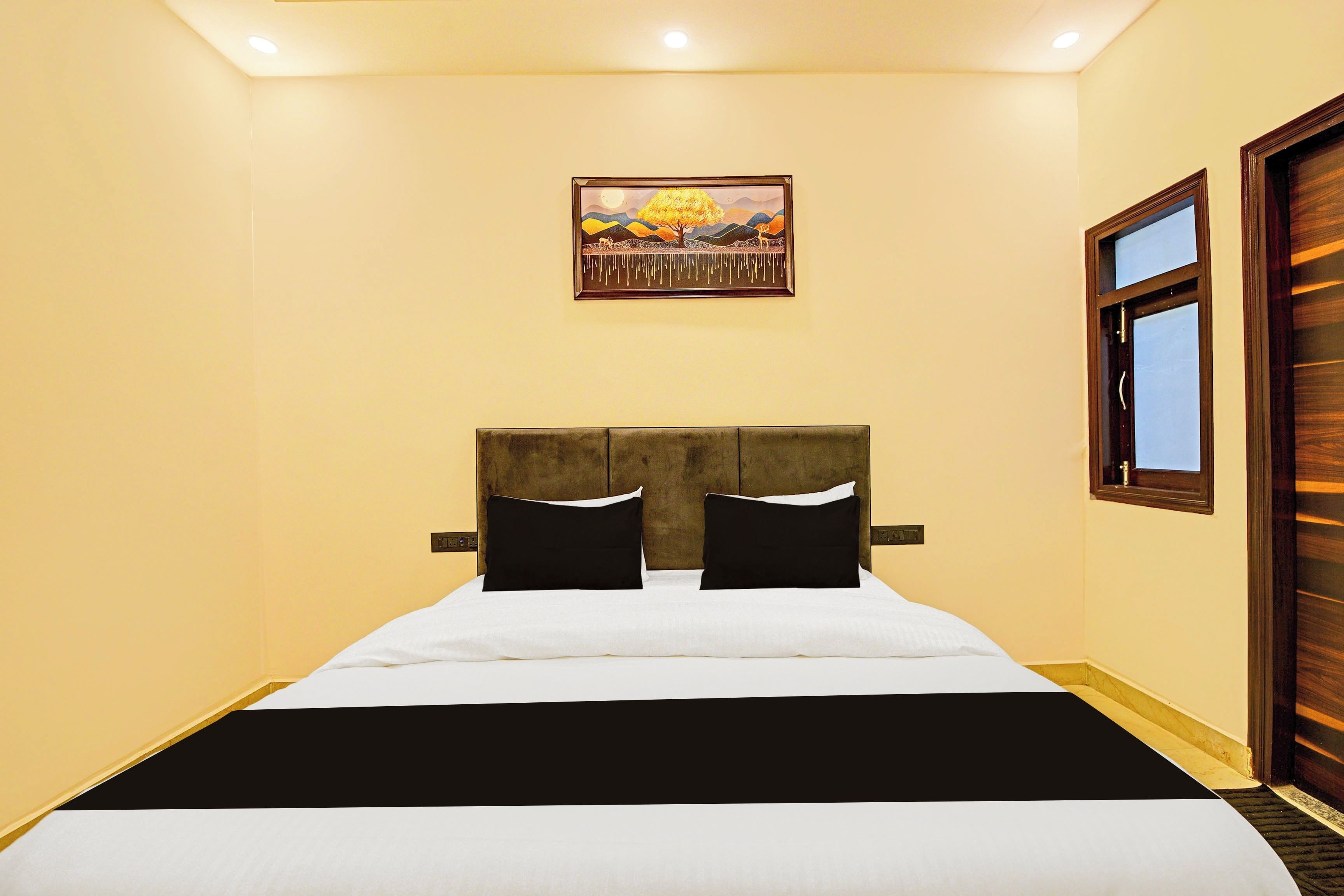 Quarto de hotel com cama, um quadro na parede e uma janela.