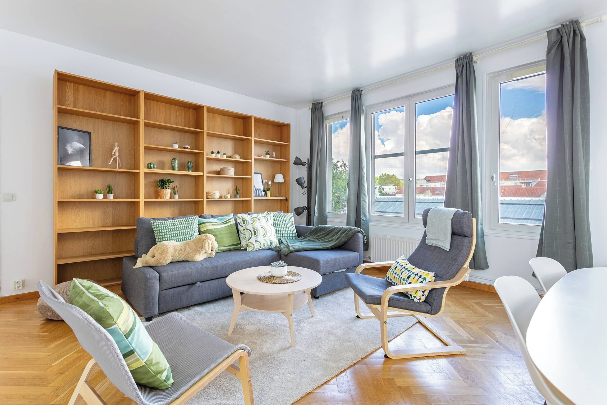 A modern living room with a sofa, chairs, a coffee table, and a large wooden bookshelf.