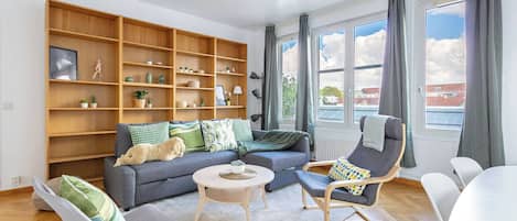 A modern living room with a sofa, chairs, a coffee table, and a large wooden bookshelf.
