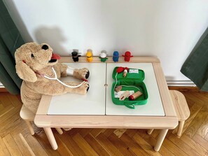 Ein Teddybär mit Stethoskop auf einem kleinen Holztisch, neben ihm ein grünes Medizinkoffer.