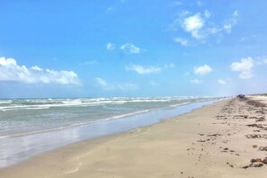 A beach with a clear sky, waves, and a distant figure. - Cici's Hideaway | Stunning Outdoor Spaces, Game Room (Corpus Christi)