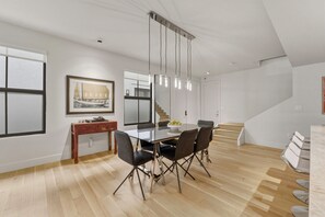 Un espace repas moderne avec un plancher en bois, une table à plateau en verre et des chaises noires. Un escalier mène à un niveau supérieur.