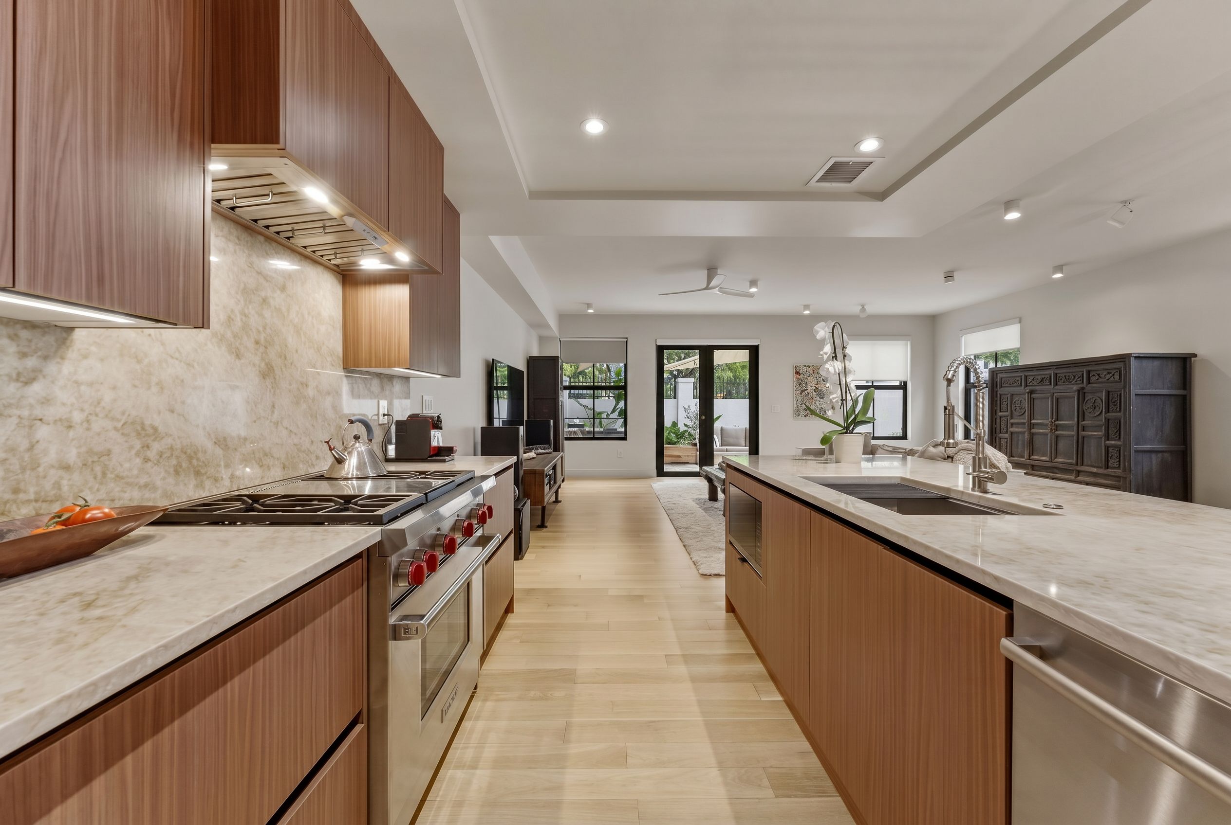 A modern kitchen with a central island, stainless steel appliances, wooden cabinetry, and a view to the outdoors.