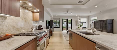 A modern kitchen with a central island, stainless steel appliances, wooden cabinetry, and a view to the outdoors.