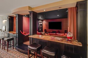 A bar area with stools, a red sofa, a bookshelf, and a flat-screen TV. - Asheville Mountain Lodge by Biltmore; Creek, Hot Tub, Theater & Games (Asheville)