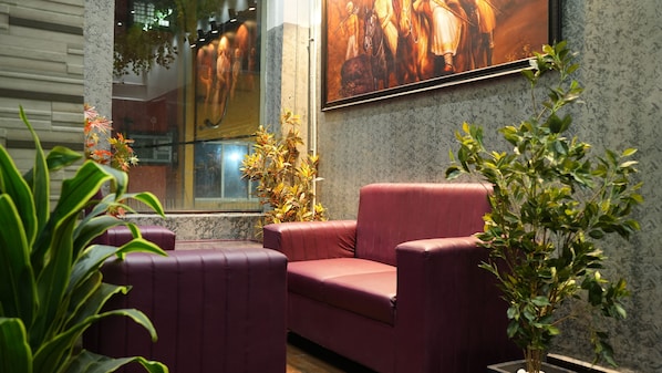 A seating area with a cushioned sofa and a potted plant. - Hotel Pavithraa Edition (Bengaluru)