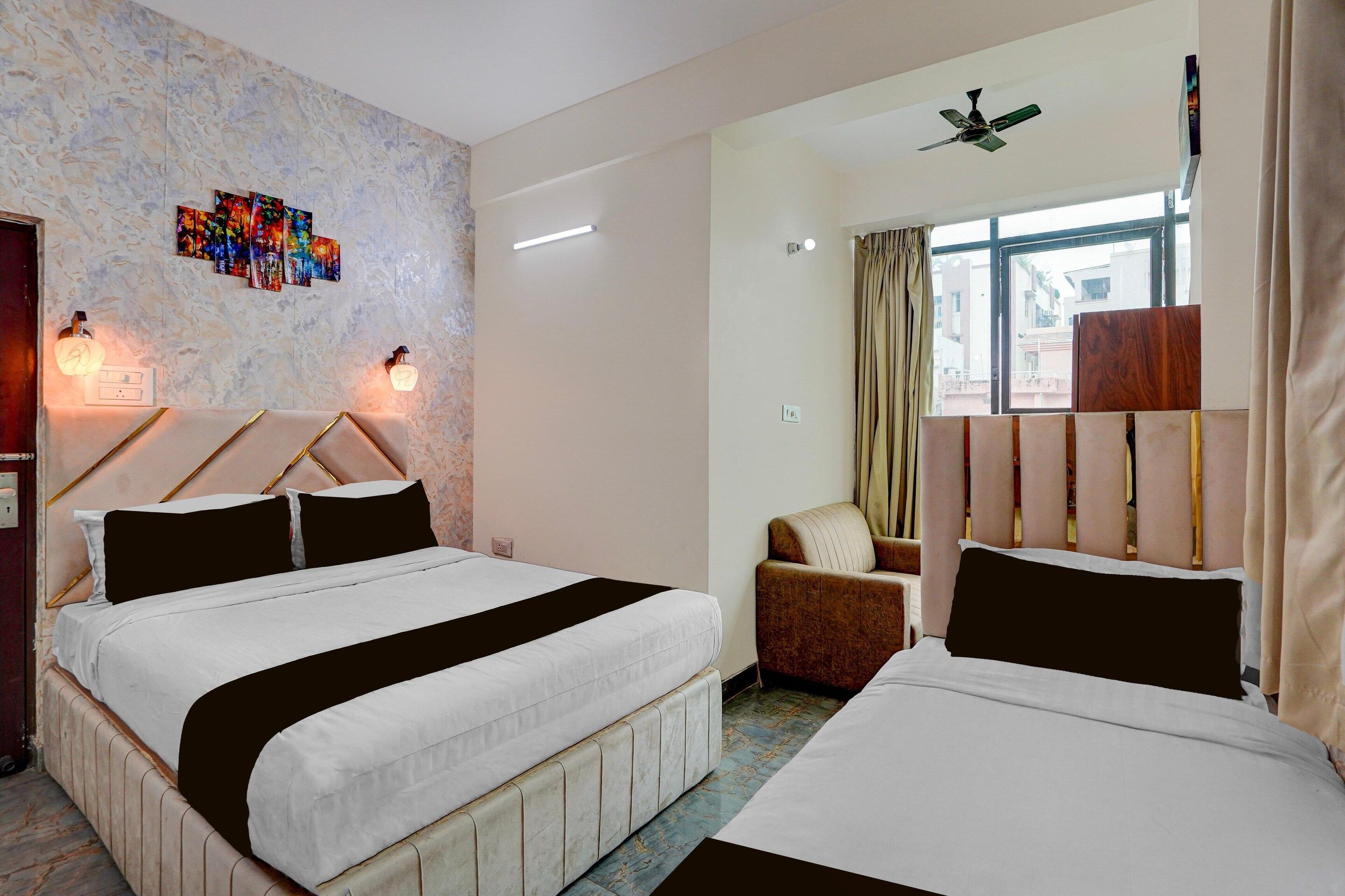 A hotel room with two beds, a ceiling fan, a window with curtains, and a wall with a light fixture and artwork.