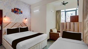 A hotel room with two beds, a ceiling fan, a window with curtains, and a wall with a light fixture and artwork.
