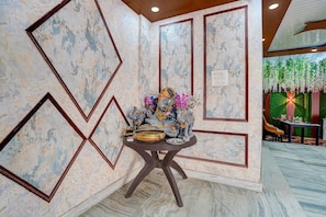 Una habitación con pared de mármol, una mesa con adornos y una pared verde con plantas colgantes.