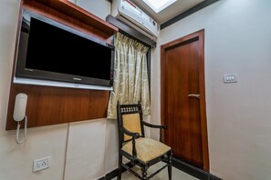 A room with a mounted television, a telephone, a wooden door, and a window with curtains.