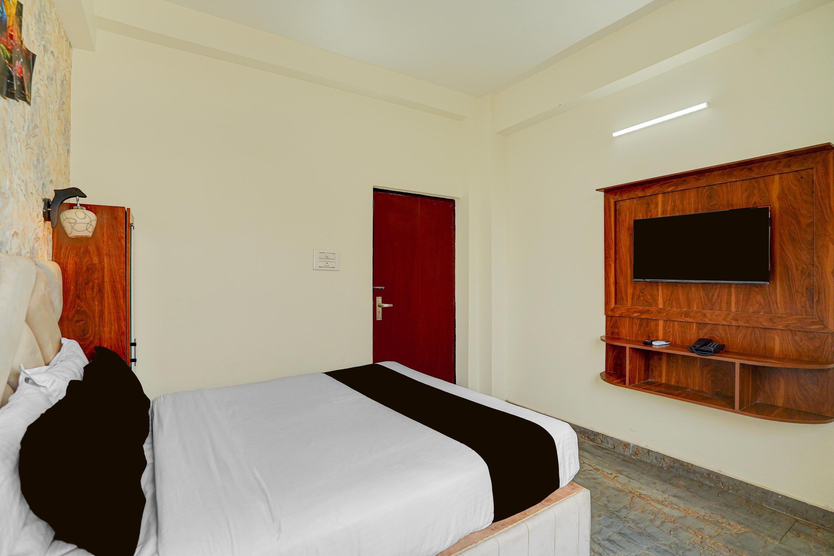Una habitació d'hotel amb un llit, una porta vermella, un televisor penjat i una prestatgeria de fusta.