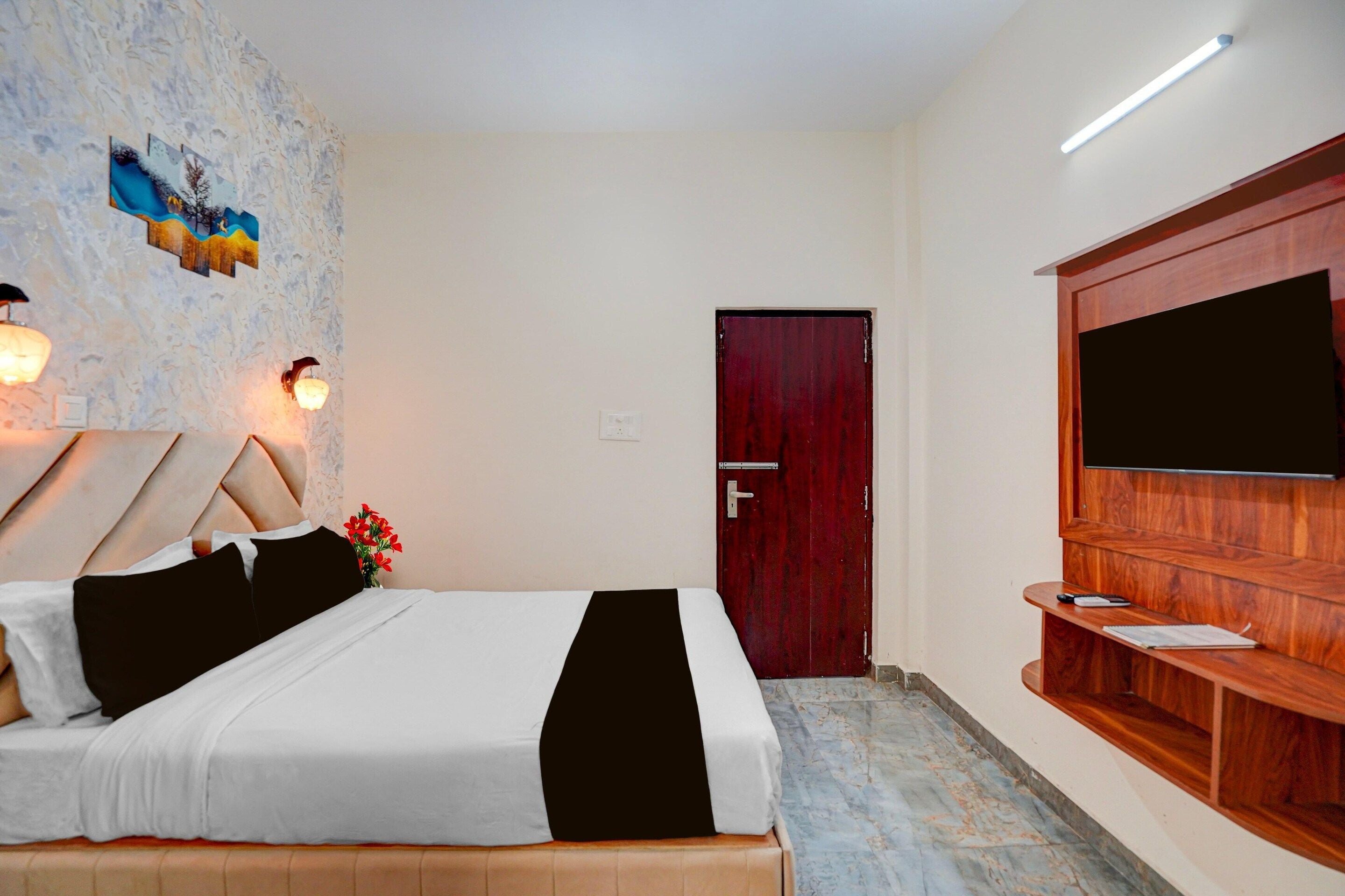 Una habitación de hotel con cama, televisor montado en la pared, banco de madera y una puerta.