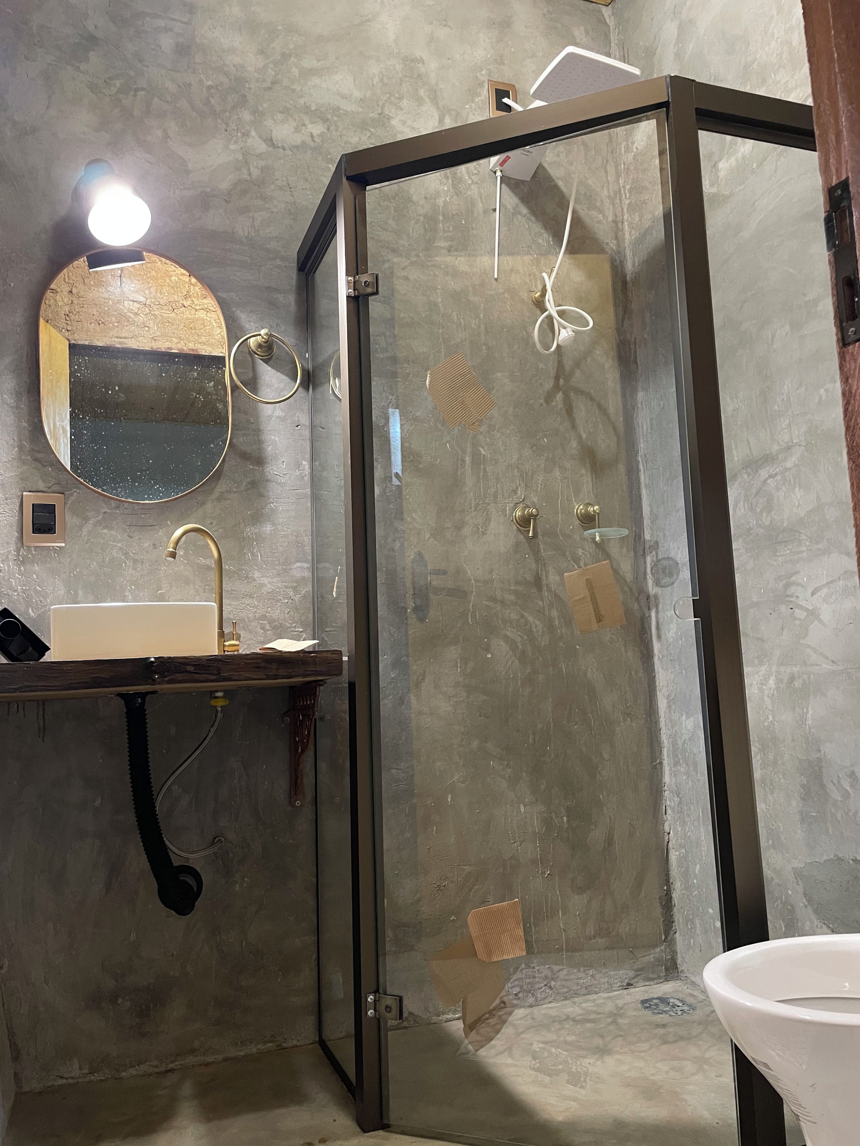 Ein Badezimmer mit einer Duschkabine aus Glas, einem Waschbecken mit goldenem Wasserhahn und einem Spiegel mit rundem Rahmen.