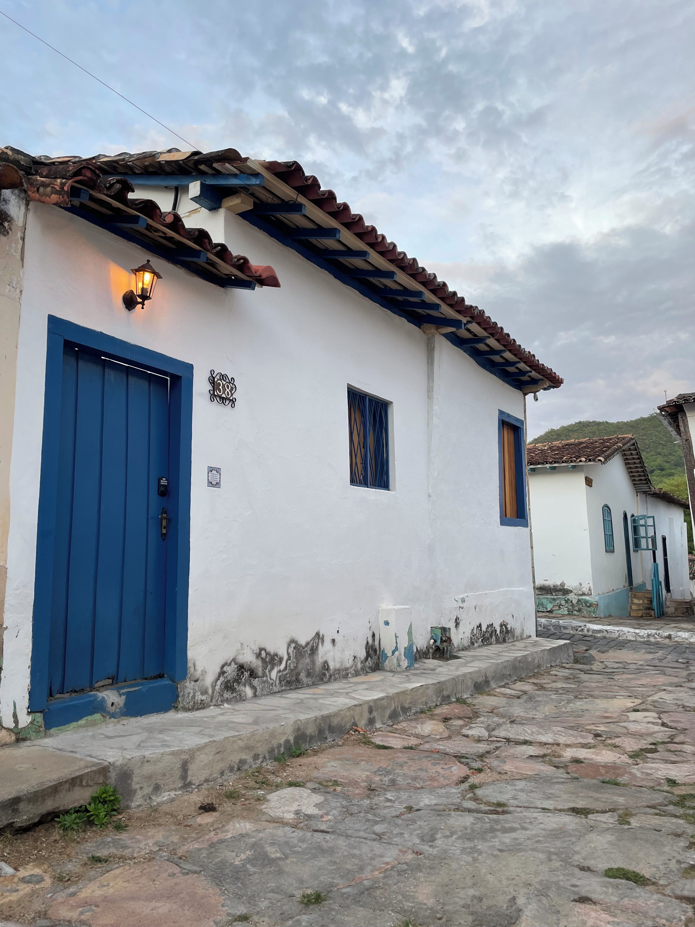 A white building with a blue door and window shutters, a stone-paved street, and a clear sky.