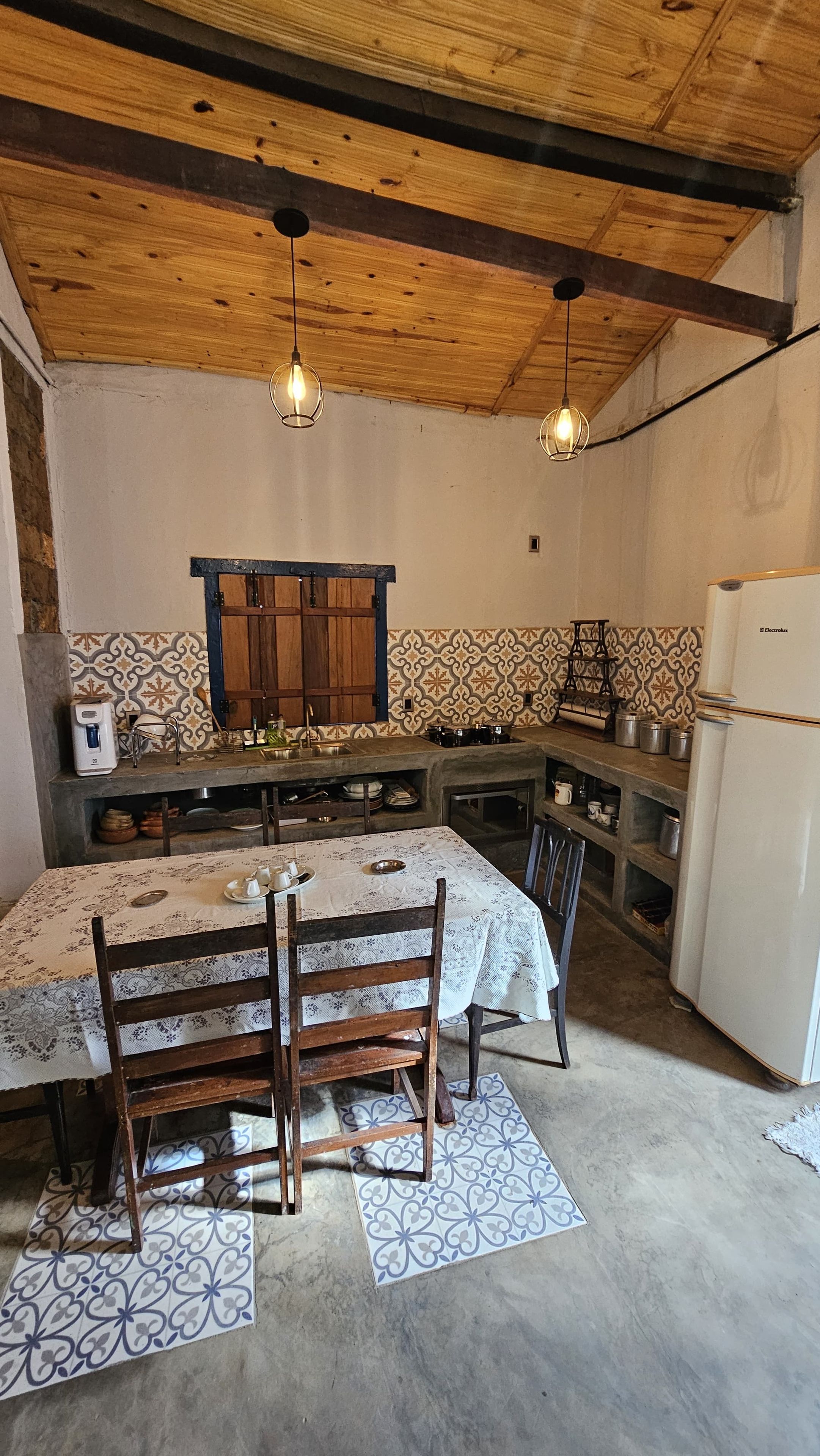 Cozinha rústica com teto de madeira, mesa de jantar com cadeiras e geladeira.