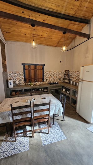 A rustic kitchen with a wooden ceiling, a dining table with chairs, and a refrigerator.