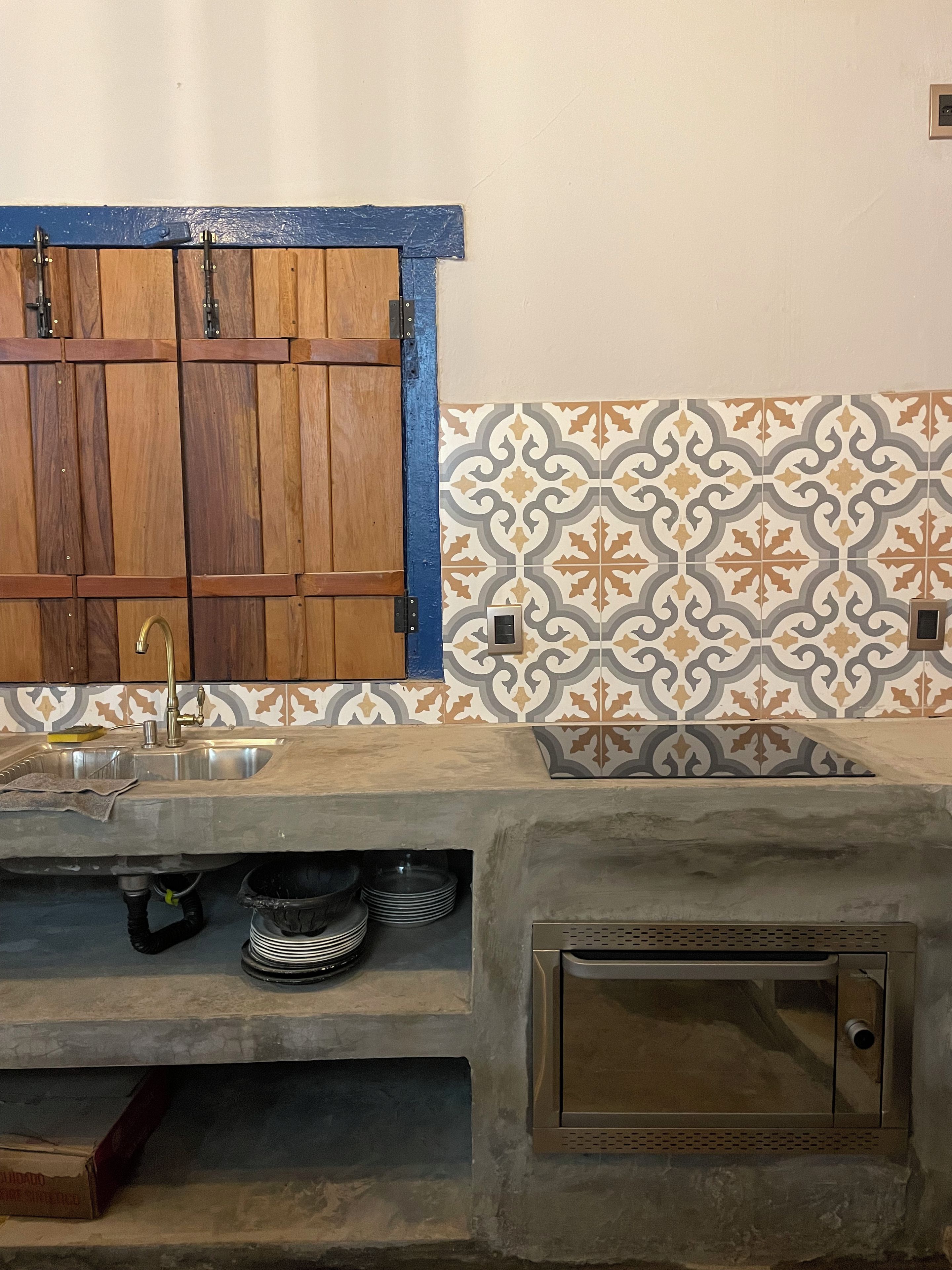 Cozinha com armário de madeira, pia e azulejos estampados.