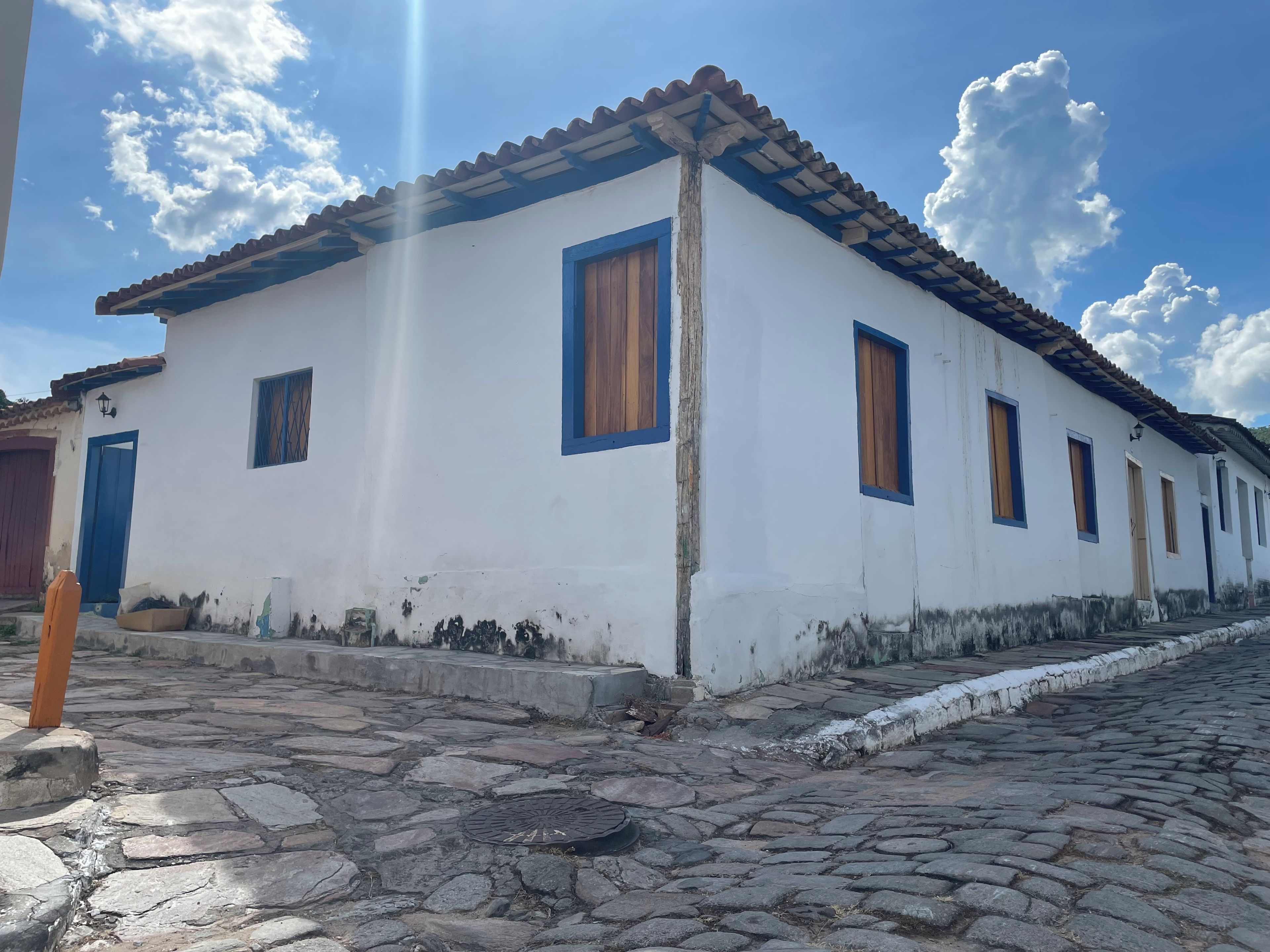 Um edifício branco com detalhes azuis e telhado ladrilhado, localizado em rua de calçamento.