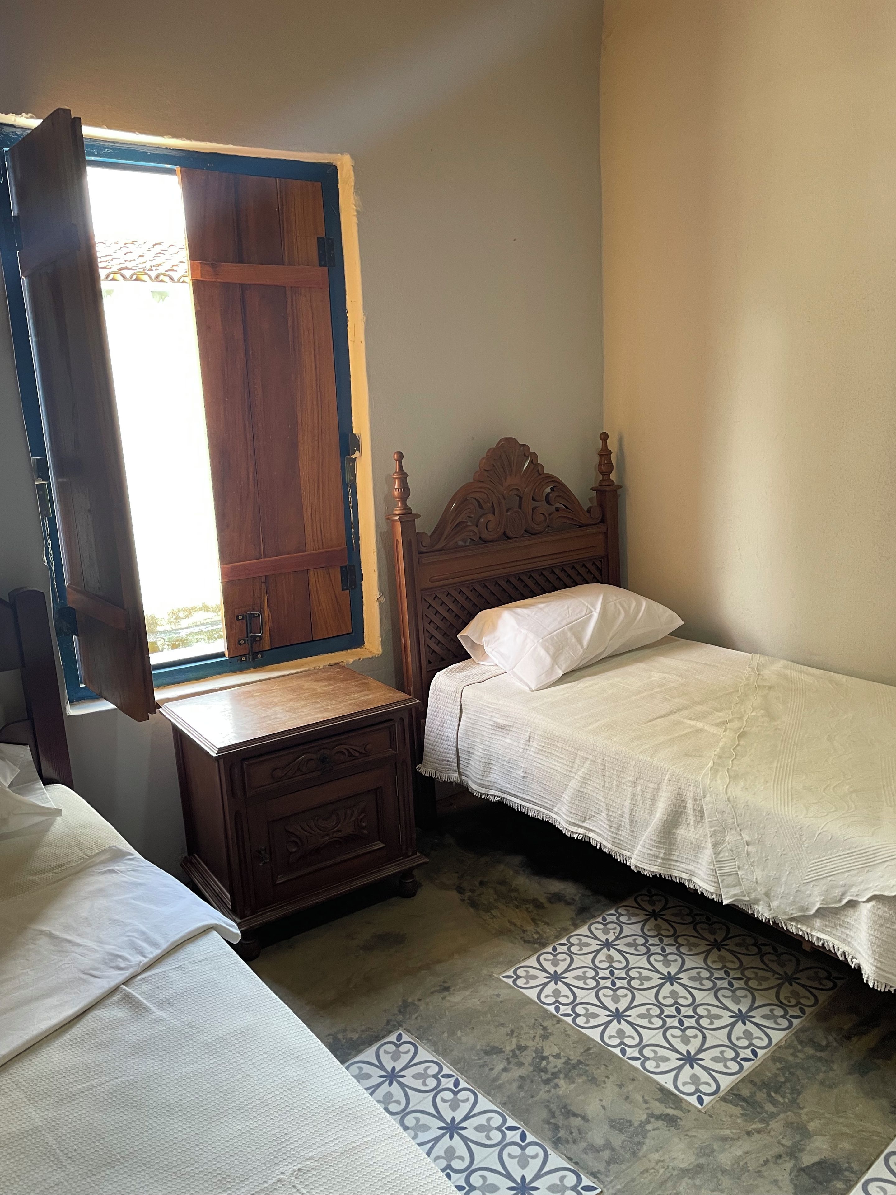A bedroom with a wooden bed, a nightstand, and a window with a wooden frame.