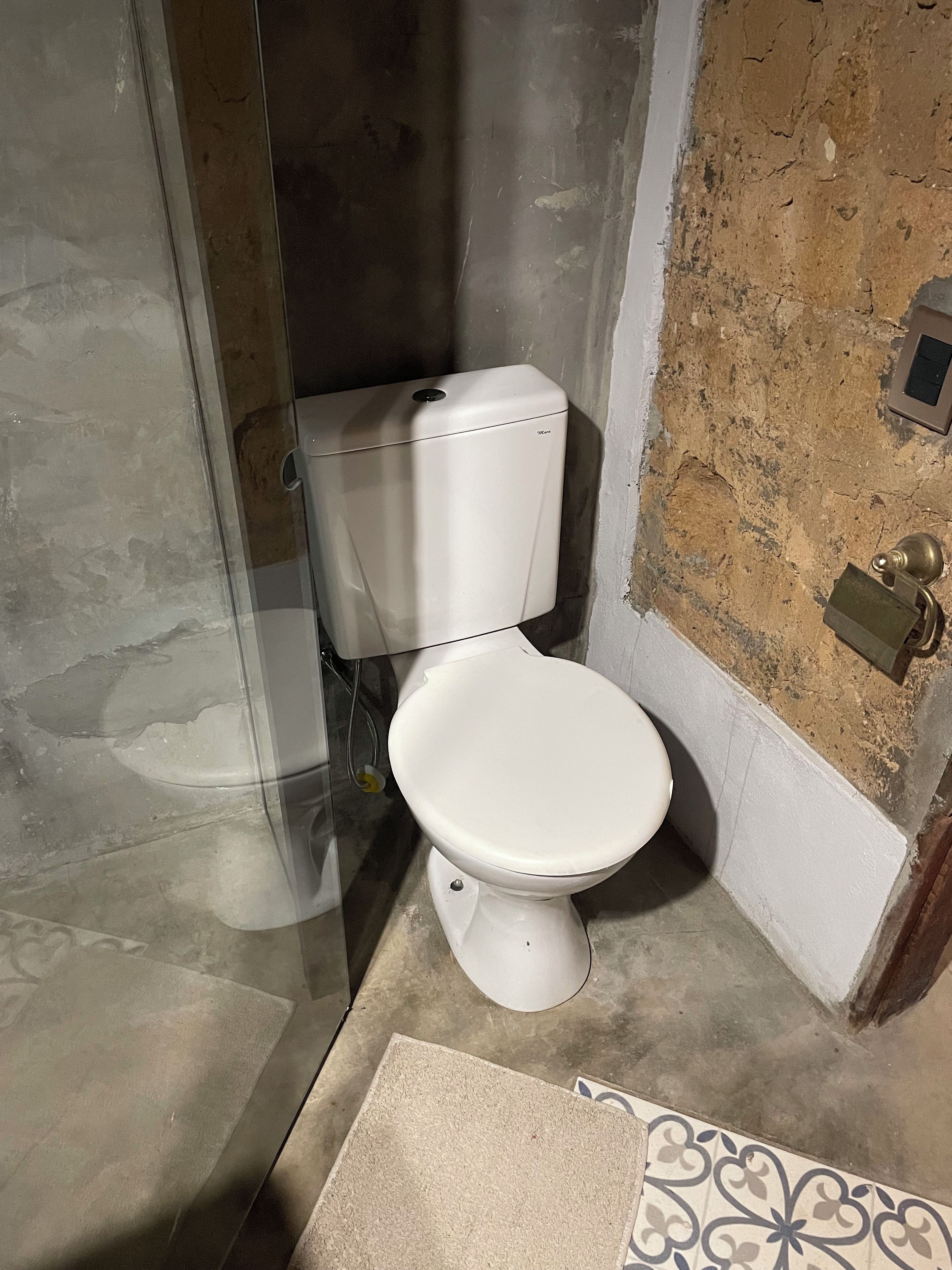 A bathroom with a white toilet, a glass shower enclosure, and a patterned floor.
