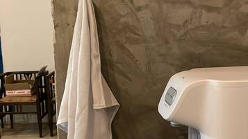 A bathroom with a stone wall, a towel hanging on a hook, a glass of water, and a white faucet.
