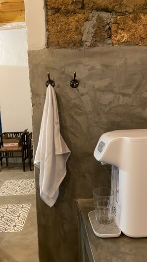 A bathroom with a stone wall, a towel hanging on a hook, a glass of water, and a white faucet. - Nice House (Historic Center) (Goiás)