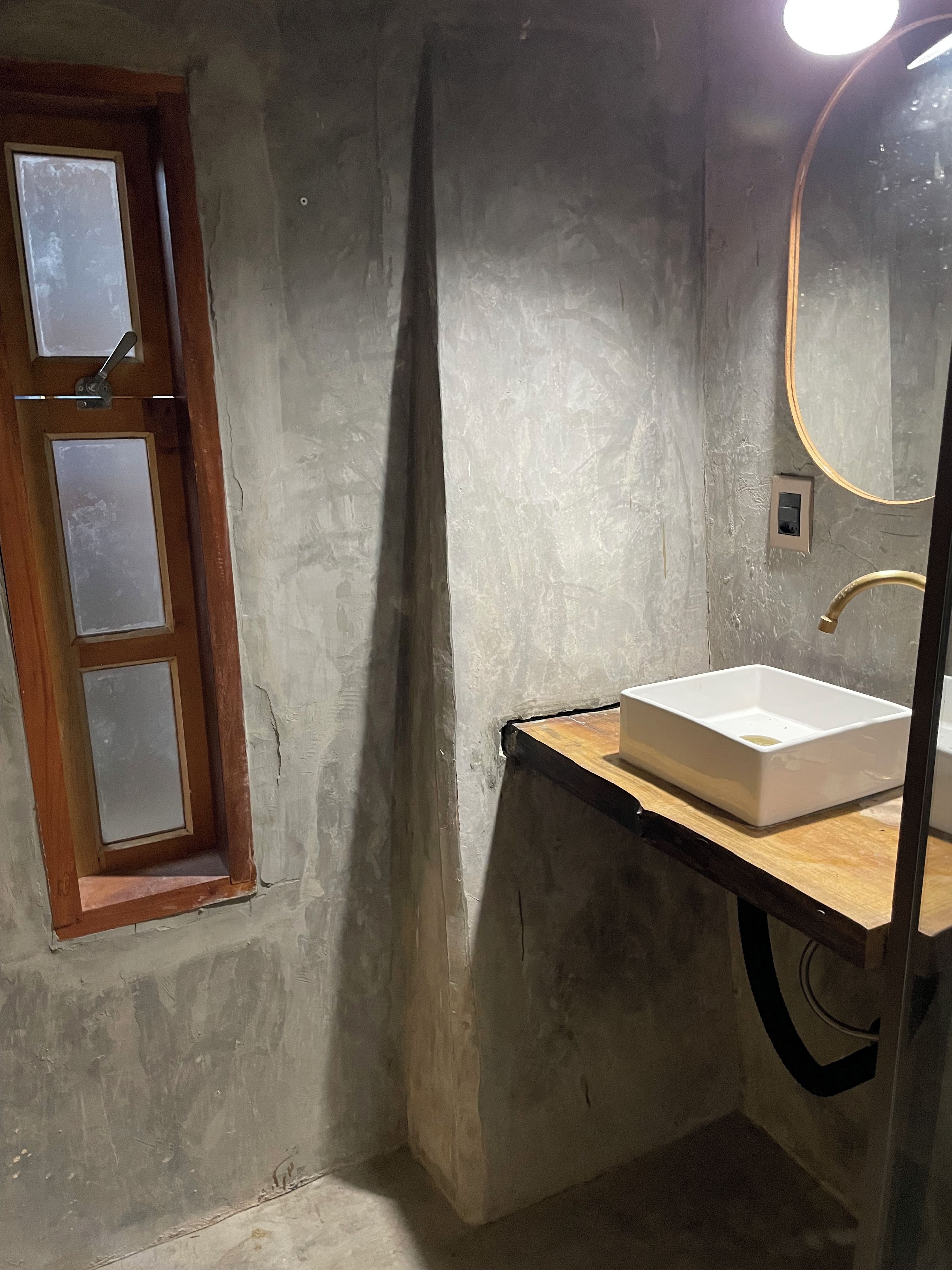 A bathroom with a wooden vanity, a white sink, a mirror, and a window with frosted glass.