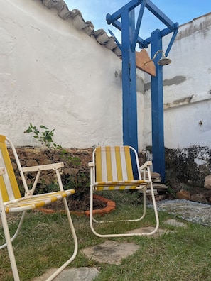 Dos sillas al aire libre con rayas amarillas y blancas, una estructura metálica azul y un muro de piedra.