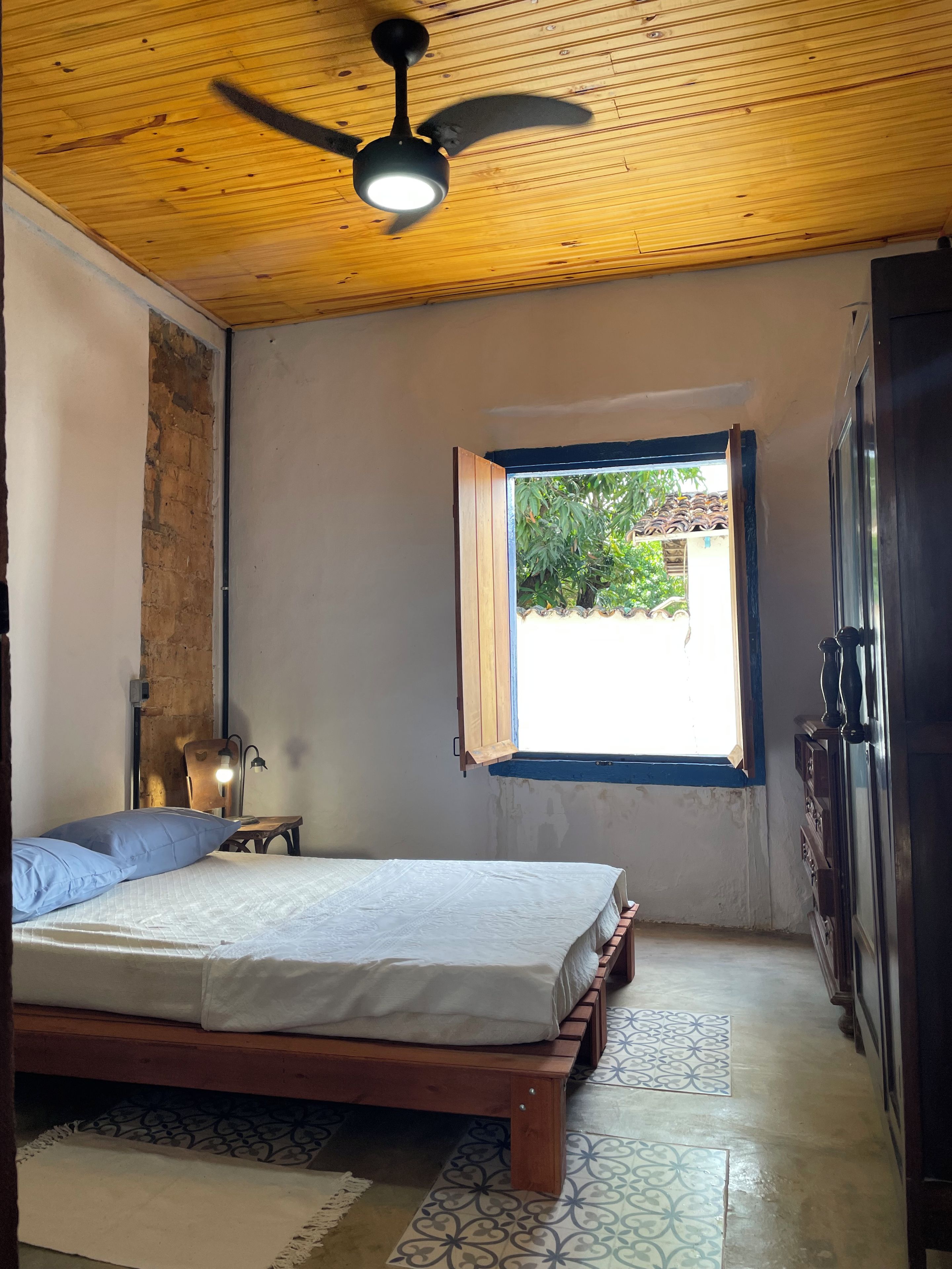 A bedroom with a bed, a ceiling fan, a window, and a wardrobe.