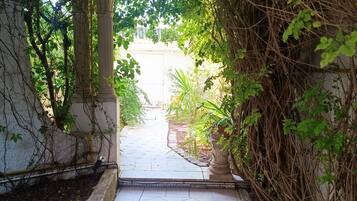 Un chemin dallé traverse un jardin, avec une structure en forme de colonne d’un côté et un feuillage dense de l’autre.