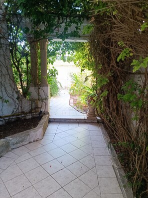 Un sendero empedrado que atraviesa un jardín con una estructura de columnas a un lado y follaje denso al otro.