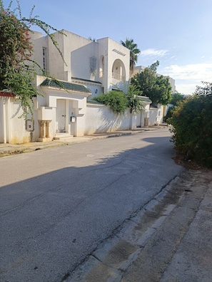 Una calle tranquila bordeada de edificios blancos, algunos con balcones y plantas.