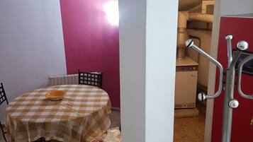 A room with a checkered table, chairs, a radiator, and a kitchenette area.