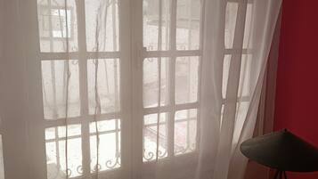 A room with a window covered by sheer curtains, a chair, and a table with a lamp.