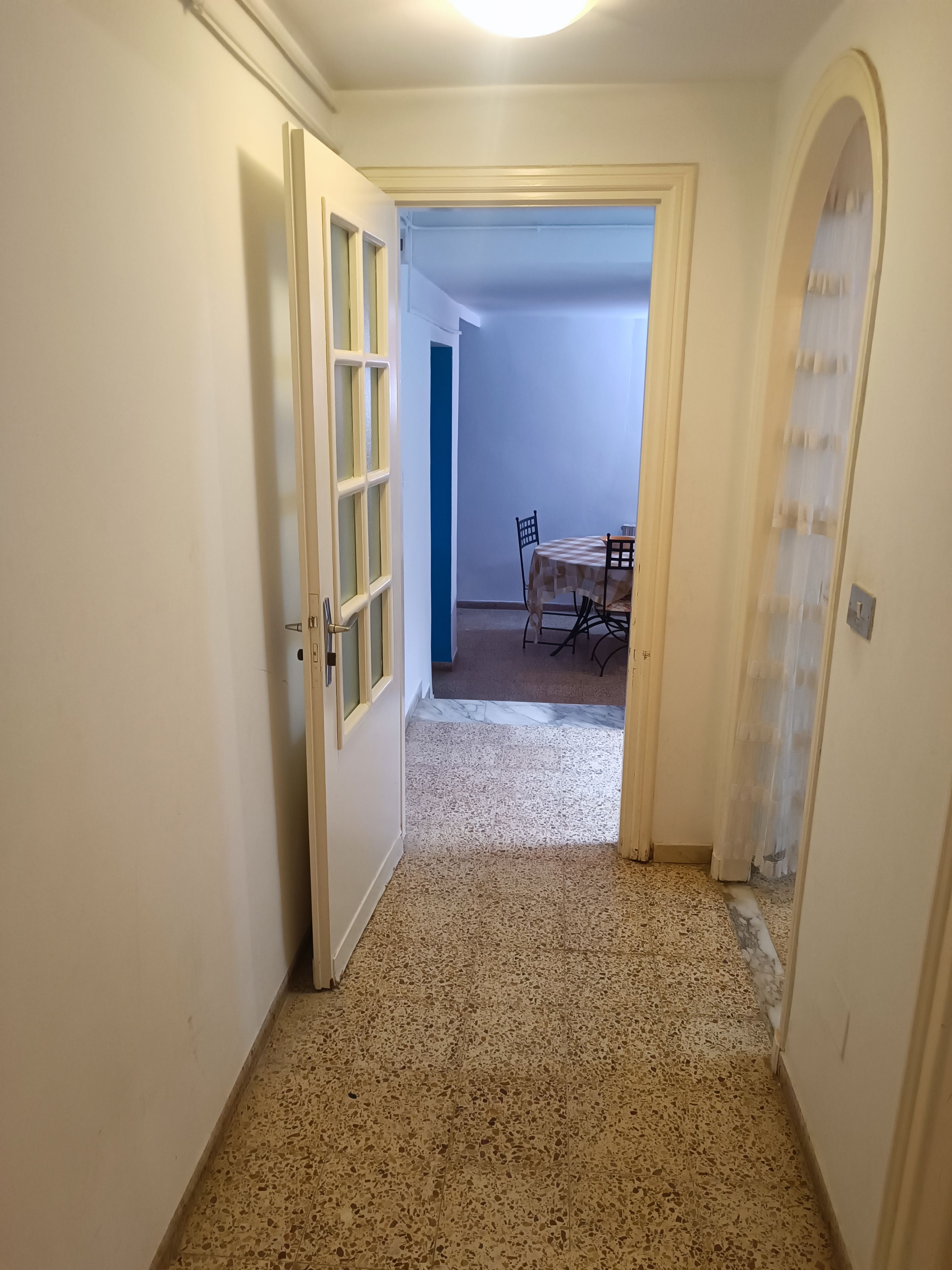A hallway with a tiled floor leading to a dining area with a table and chairs.