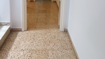 Un pasillo con piso de terrazo que conduce a una habitación con puerta oscura.