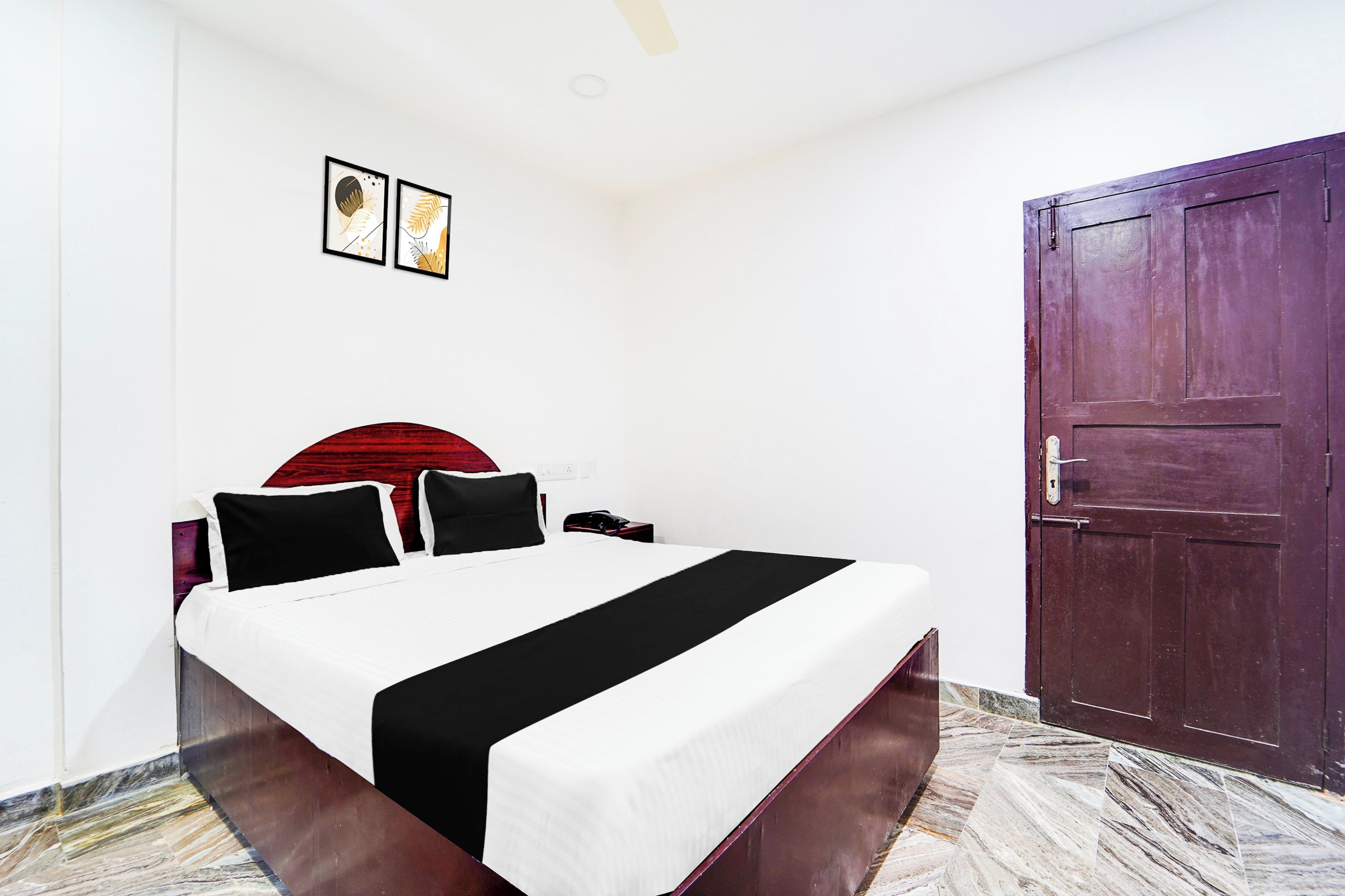 A hotel room with a bed, a nightstand, a telephone, a door, and two framed pictures on the wall.
