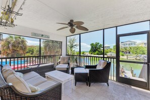 Ein sonniger Balkon mit Korbmöbeln, einem Deckenventilator und Blick auf Pool und Strand.