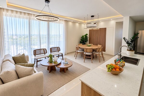 A modern living room with a sofa, dining table, and kitchen area with fruit bowl.