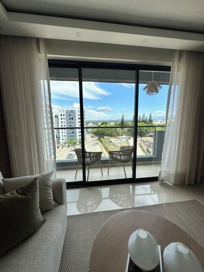 Ein modernes Wohnzimmer mit großem Fenster, einer Couch, einem Couchtisch und Blick auf die Skyline.